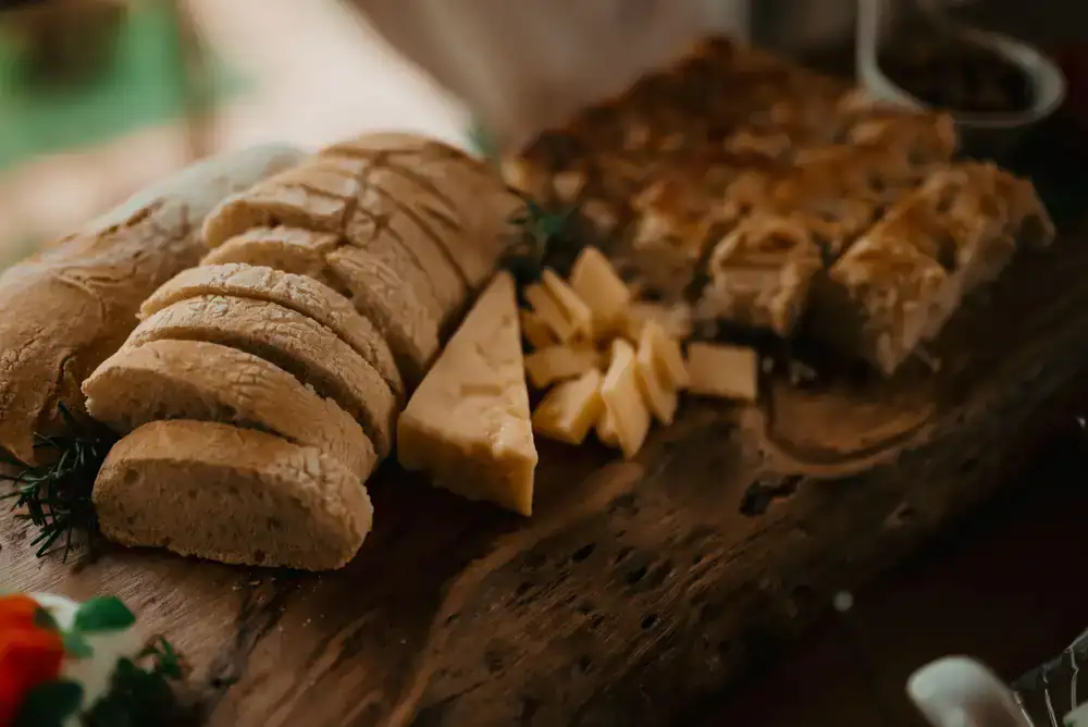 A large wooden board displaying various cut cheeses with rustic bread